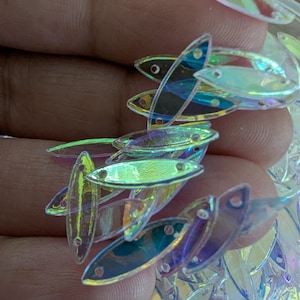 May include: A close-up of a pile of iridescent oval-shaped sequins. The sequins are translucent and have a rainbow sheen.