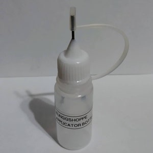 May include: A small, clear plastic applicator bottle with a white cap and a thin, black needle. The bottle has a label that reads "BLINGGSHOPPE APPLICATOR BOTTLE". A clear plastic tube is attached to the cap.