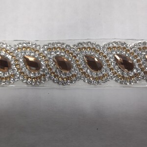 May include: A silver and gold trim with clear and gold rhinestones and a row of teardrop-shaped, rose gold-colored rhinestones.