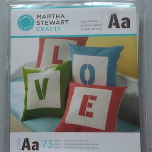 Puede incluir: Un paquete de 36 plantillas de papel para manualidades. Las plantillas miden 19,1 cm x 19,1 cm y presentan letras del alfabeto. El paquete est&aacute; etiquetado como "Martha Stewart Crafts" e incluye el texto "Aa 73 dise&ntilde;os".