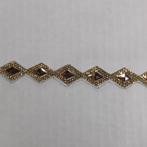 May include: A gold trim with a row of diamond-shaped rhinestones. The rhinestones have a clear center and a gold border.