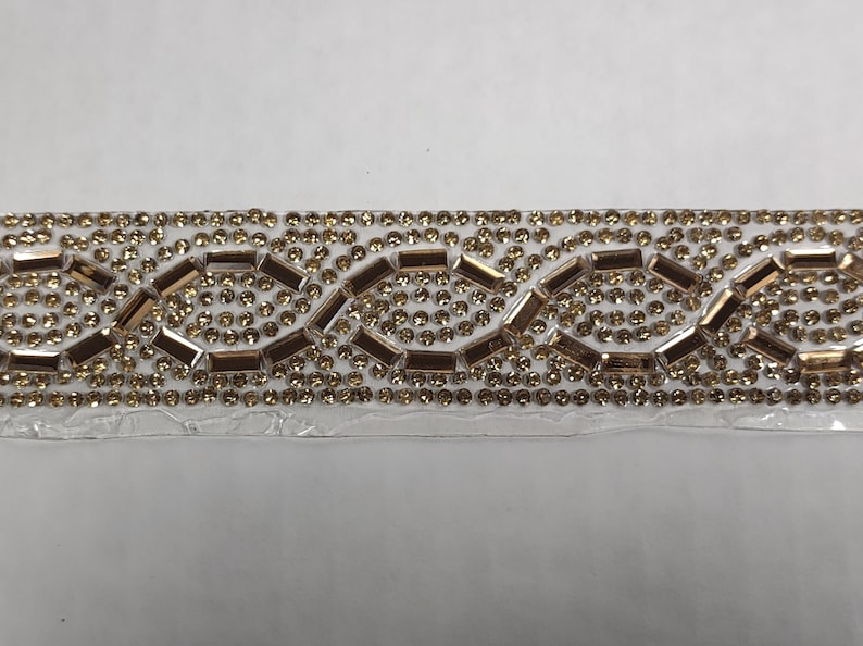 May include: A gold and clear rhinestone trim with a repeating pattern of small and large rhinestones.