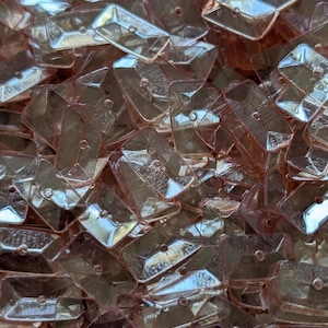 May include: A pile of translucent, iridescent, light pink, rectangular sequins with a hole in the center.