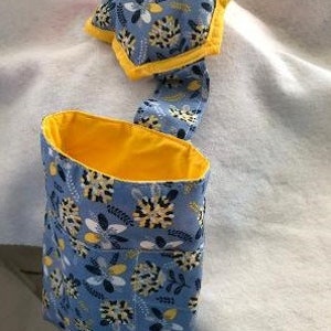 Puede incluir: Un cubo de basura de tela azul y amarillo con un patrón floral. El cubo tiene un forro amarillo y una tapa de tela azul y amarillo a juego.
