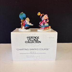 May include: A set of two handpainted porcelain figurines titled Charting Santa's Course from The Heritage Village Collection. One figurine shows a figure with a globe, the other a figure with a telescope on books, both atop a white box.