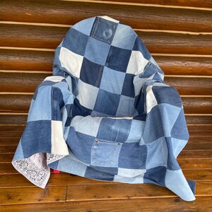 May include: A patchwork quilt constructed from various shades of blue denim fabric squares. The design features multiple integrated denim pockets and a corner section accented with a white and black patterned bandana fabric, creating a textured look.