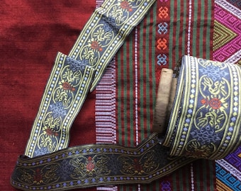 May include: Close-up of a gray and gold trim ribbon with a floral pattern. The ribbon is on a red and green striped fabric.