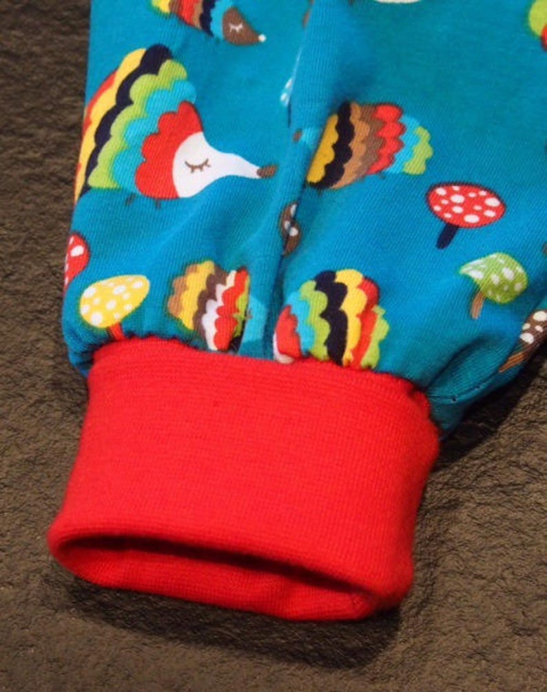 May include: Red and blue fabric with a colorful hedgehog pattern. The fabric has a red cuff at the bottom.