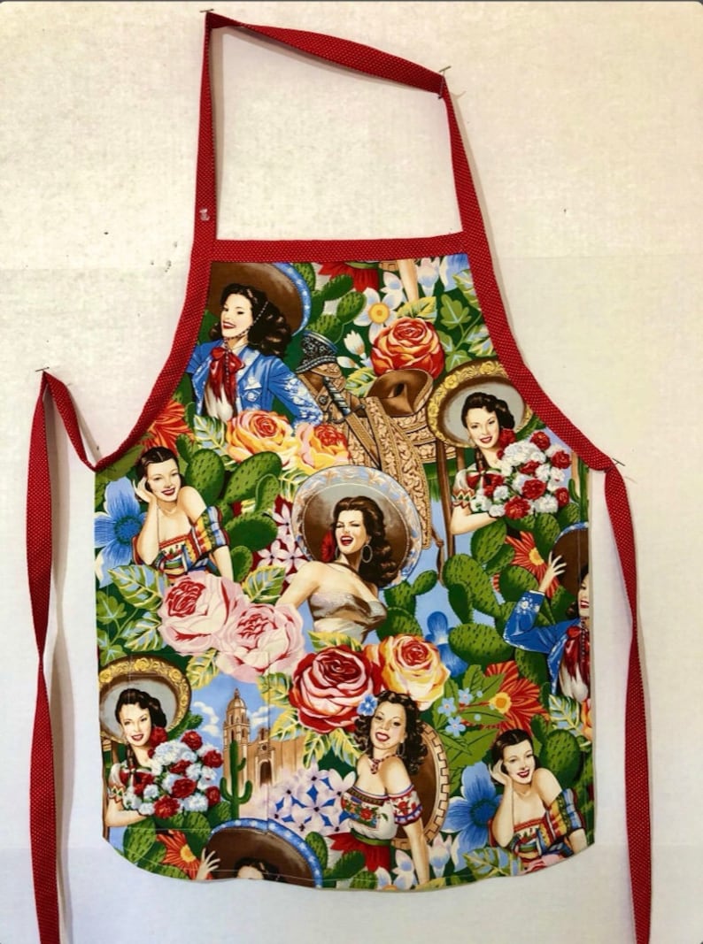 May include: Red and white apron with a colorful floral print featuring women in sombreros and cacti.