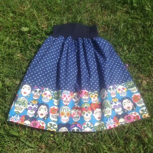 May include: A blue and white polka dot skirt with a colorful skull print on the bottom. The skirt has a wide elastic waistband.