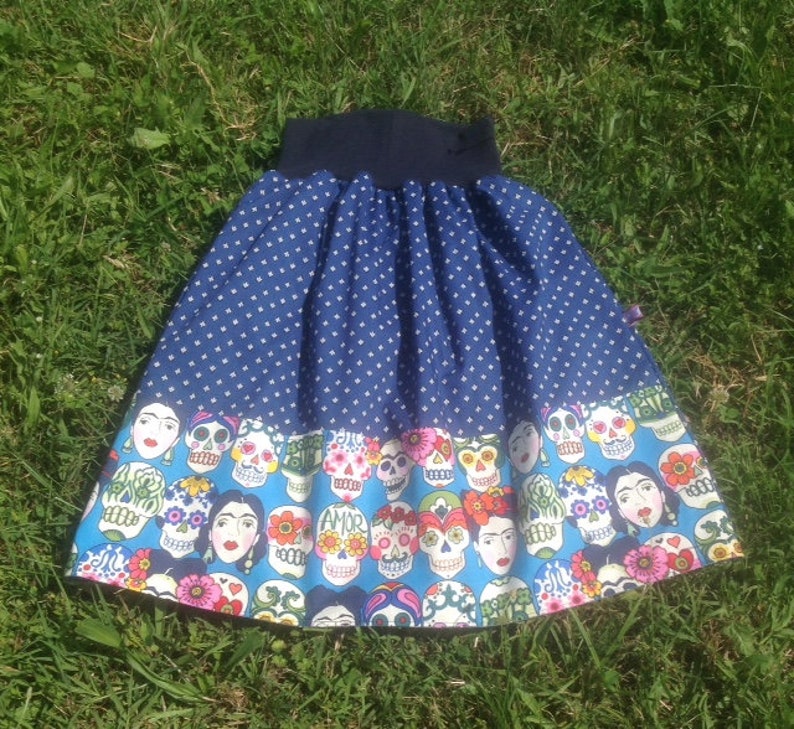 May include: A blue and white polka dot skirt with a colorful skull print on the bottom. The skirt has a wide elastic waistband.