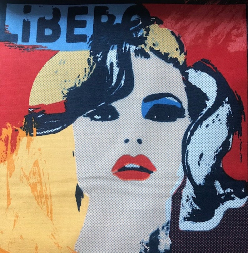 May include: A colorful pop art style image of a woman's face with the word "LIBERO" in blue letters across the top. The woman has blue eyeshadow, red lipstick, and black hair. The background is red, yellow, and blue.