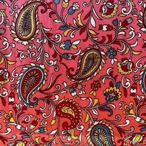 Op de afbeelding: Een roze stof met een paisley-patroon. Het patroon bevat ingewikkelde swirls, bladeren en bloemen in tinten rood, blauw, geel en bruin.