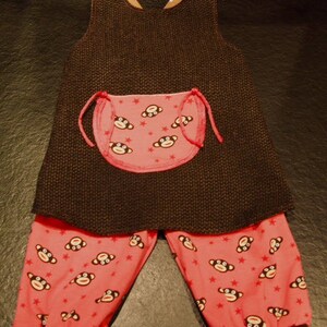 May include: A brown and pink baby overall with a monkey print on the bib and pants. The overall has a brown knit fabric and the pants are a pink cotton fabric.
