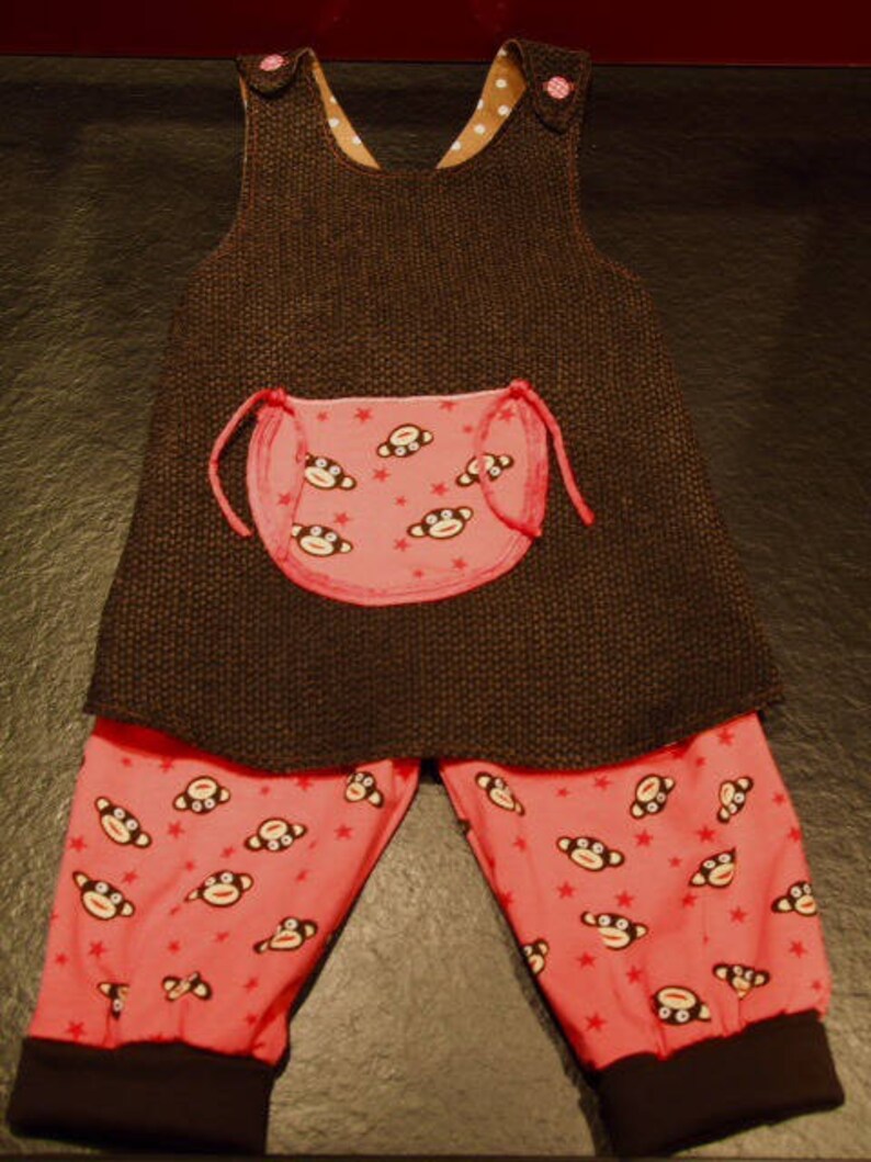 May include: A brown and pink baby overall with a monkey print on the bib and pants. The overall has a brown knit fabric and the pants are a pink cotton fabric.