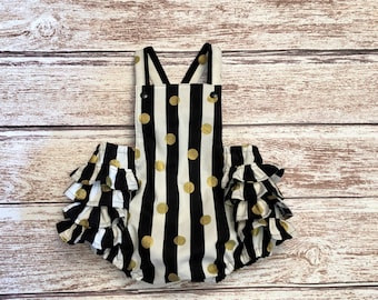 May include: Black and white striped baby romper with gold polka dots and a ruffled hem.