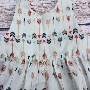 May include: A white sleeveless dress with a pattern of colorful arrows. The dress has a gathered skirt and a simple neckline.
