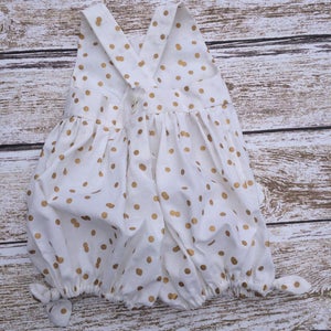 May include: White baby onesie with gold polka dots and a criss-cross strap back.