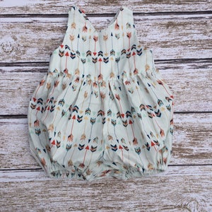 May include: A white baby onesie with a pattern of colorful arrows. The onesie has a sleeveless design and a gathered skirt.