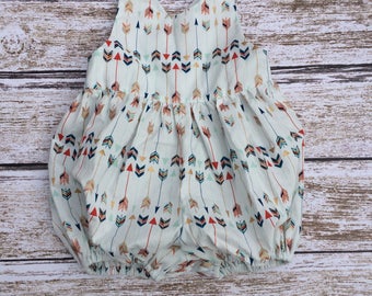 May include: A white baby onesie with a pattern of colorful arrows. The onesie has a sleeveless design and a gathered skirt.