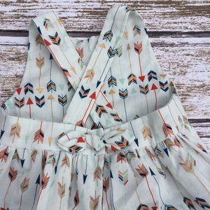 May include: A white sleeveless dress with a criss-cross back and a bow tie at the waist. The dress is covered in a pattern of colorful arrows.