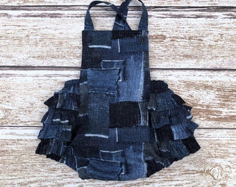 May include: A blue denim baby overall with a ruffled skirt. The overall has a patchwork design and is made of a soft, comfortable fabric.
