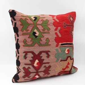 May include: Square cushion with a woven, patterned design. The cushion features a colour palette of red, green, black, and beige. The design includes geometric shapes and floral motifs, creating a textured appearance.