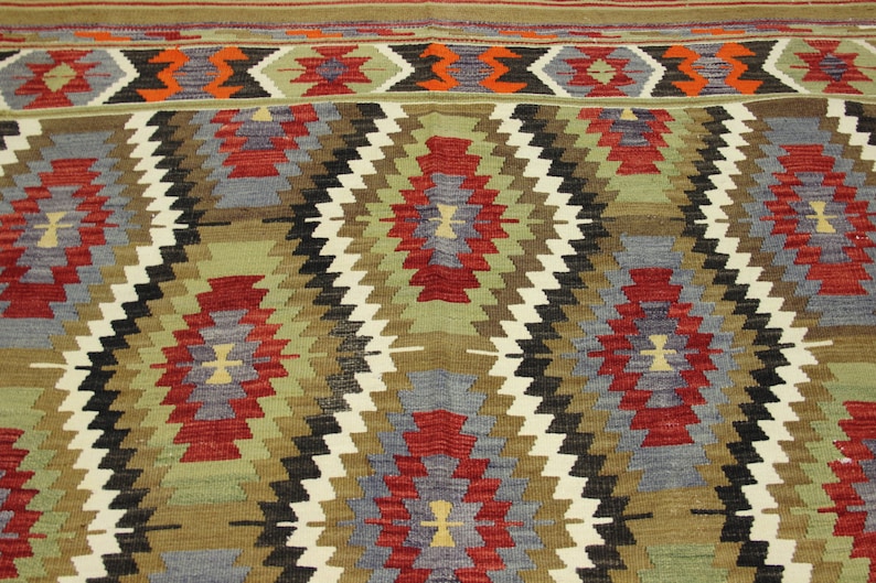 May include: A traditional rug with a geometric pattern in shades of red, blue, green, brown, and white. The rug has a woven texture and a diamond-shaped design.