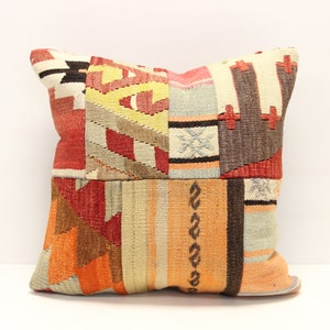 Könnte beinhalten: Ein Patchwork-Kissenbezug mit einem geometrischen Muster in Rot-, Orange-, Braun- und Beigetönen. Der Kissenbezug ist aus gewebtem Stoff und hat einen Fransenrand.