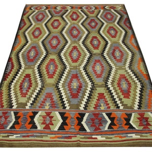 May include: A traditional rug with a geometric pattern in shades of red, green, black, and white. The rug has a diamond-shaped design with a border of smaller geometric shapes.