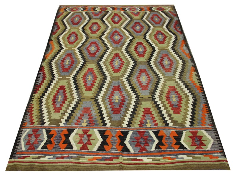 May include: A traditional rug with a geometric pattern in shades of red, green, black, and white. The rug has a diamond-shaped design with a border of smaller geometric shapes.