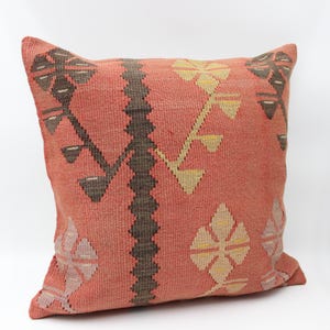Puede incluir: Un cojín cuadrado tejido de color coral con un patrón geométrico. El diseño presenta formas marrón oscuro, beige y marrón claro. El cojín está probablemente hecho de una tela duradera, adecuada para uso decorativo en un sofá o cama.
