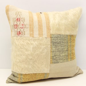 Op de afbeelding: Een vierkant patchwork kussen met verschillende texturen en kleuren, waaronder wit, beige, bruin en geel. Het kussen is gemaakt van verschillende stoffen, waaronder een pluche witte stof, een gestreepte stof en een gepatenteerde stof.
