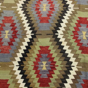 May include: A close-up of a woven rug with a geometric pattern in shades of red, green, blue, and brown.
