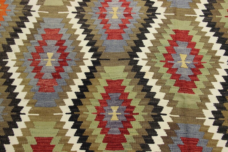 May include: A close-up of a woven rug with a geometric pattern in shades of red, green, blue, and brown.