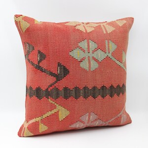May include: A square, red cushion with a woven design. The cushion features a repeating pattern of floral and geometric shapes in shades of brown, beige, and light green. The cushion is made of a textured fabric.