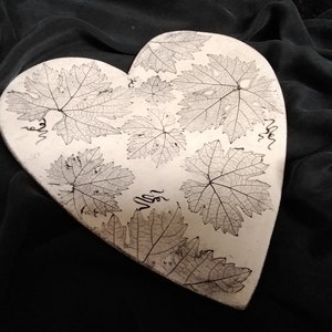 May include: White ceramic heart-shaped dish with a raised design of pressed grape leaves.