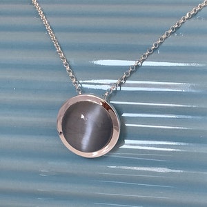 Peut inclure: Un collier en chaîne argent avec un pendentif rond orné d'une pierre grise.
