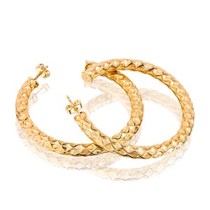 May include: A pair of gold hoop earrings with a textured diamond pattern. The earrings are large and have a polished finish.