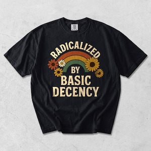 Może przedstawiać: Czarny t-shirt z krótkim rękawem z nadrukiem graficznym zawierającym napis RADICALIZED BY BASIC DECENCY kremowymi literami. Wzór zawiera wielokolorową tęczę w odcieniach pomarańczu, brązu i zieleni, otoczoną kilkoma żółtymi i brązowymi kwiatami.