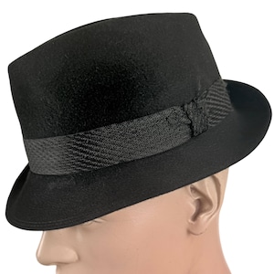 May include: A solid black fedora hat featuring a structured crown and a slightly curved brim. The hat is accented with a wide, textured black grosgrain ribbon band that includes a small, decorative knot detail on the side of the crown.