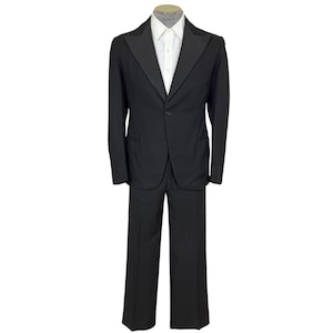 Op de afbeelding: Een zwart pak met een wit overhemd. Het pak heeft een jasje met één knoop en een revers en een bijpassende broek. Het pak wordt op een mannequin gepresenteerd tegen een witte achtergrond. Een klassiek formeel pak.