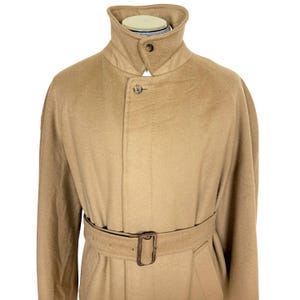 Op de afbeelding: Een beige jas van wolmix met een hoge opstaande kraag met &eacute;&eacute;n knoopsluiting, een verborgen sluiting aan de voorzijde met een zichtbare bovenste knoop en een bijpassende ceintuur met een rechthoekige gesp.
