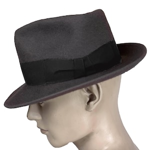 May include: A dark grey fedora hat featuring a black band. The hat has a traditional design with a gently curved brim. The hat is displayed on a mannequin head.