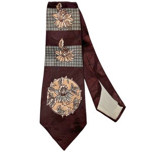 Może przedstawiać: Bordowy jedwabny krawat z geometrycznym wzorem brązowych i beżowych motywów kwiatowych. Krawat ma białą podszewkę.