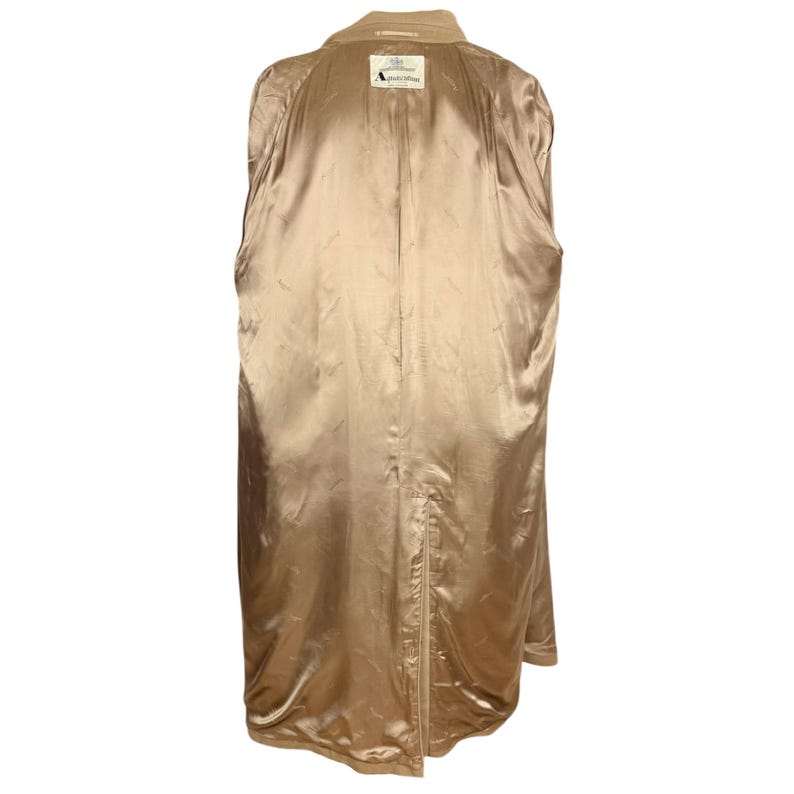 Op de afbeelding: Een beige trenchcoat gezien vanaf de binnenkant, voorzien van een gladde, satijnachtige voering in een bijpassende bruine tint. Een wit rechthoekig label bij de nek toont de tekst Aquascutum London, met een kleine split aan de onderzoom.