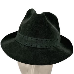 May include: A dark green fedora hat with a wide brim and a decorative band. The band has small, evenly spaced cut-out shapes. The hat is made of a soft, felt-like material. The hat's brim is approximately 30 cm in diameter.