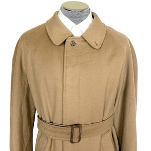 Op de afbeelding: Een beige trenchcoat van een wolmix met een klassieke kraag, een verborgen knoopsluiting met &eacute;&eacute;n zichtbare knoop aan de bovenkant en een bijpassende stoffen riem met een rechthoekige gesp, gedragen over een wit overhemd met kraag.