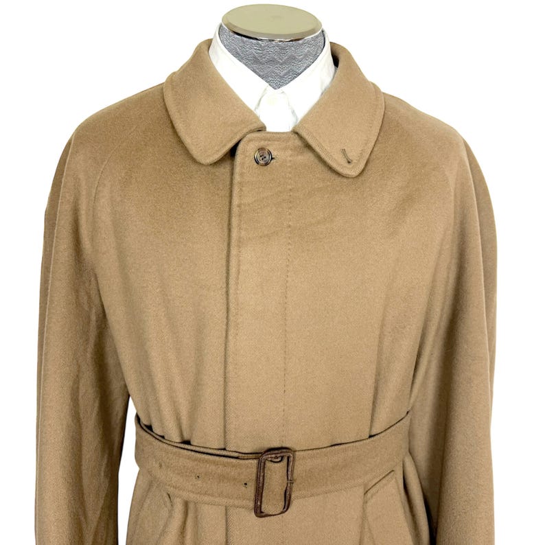 Op de afbeelding: Een beige trenchcoat van een wolmix met een klassieke kraag, een verborgen knoopsluiting met &eacute;&eacute;n zichtbare knoop aan de bovenkant en een bijpassende stoffen riem met een rechthoekige gesp, gedragen over een wit overhemd met kraag.