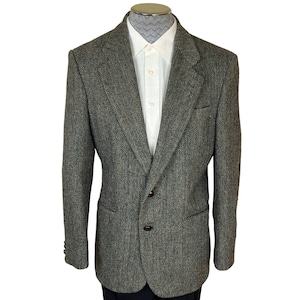 Puede incluir: Una chaqueta de tweed verde y marrón con un cierre de botón único y dos bolsillos de solapa. La chaqueta tiene un patrón de espiga y un ajuste clásico.